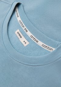 Col col de sweat-shirt en coton bleu clair avec encolure côtelée et étiquettes blanches de taille et de marque portant les inscriptions "ombre" et "cotton line".