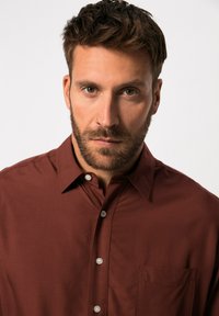 Camicia button-up di colore ruggine scuro, realizzata in tessuto morbido, con colletto a punta, tasca frontale e bottoni bianchi.