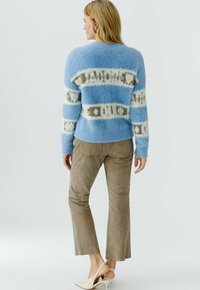 Lichtblauwe, pluizige trui met crèmekleurige en beige strepen, gecombineerd met beige suède broek en beige hoge hakken. De trui heeft een losse pasvorm.