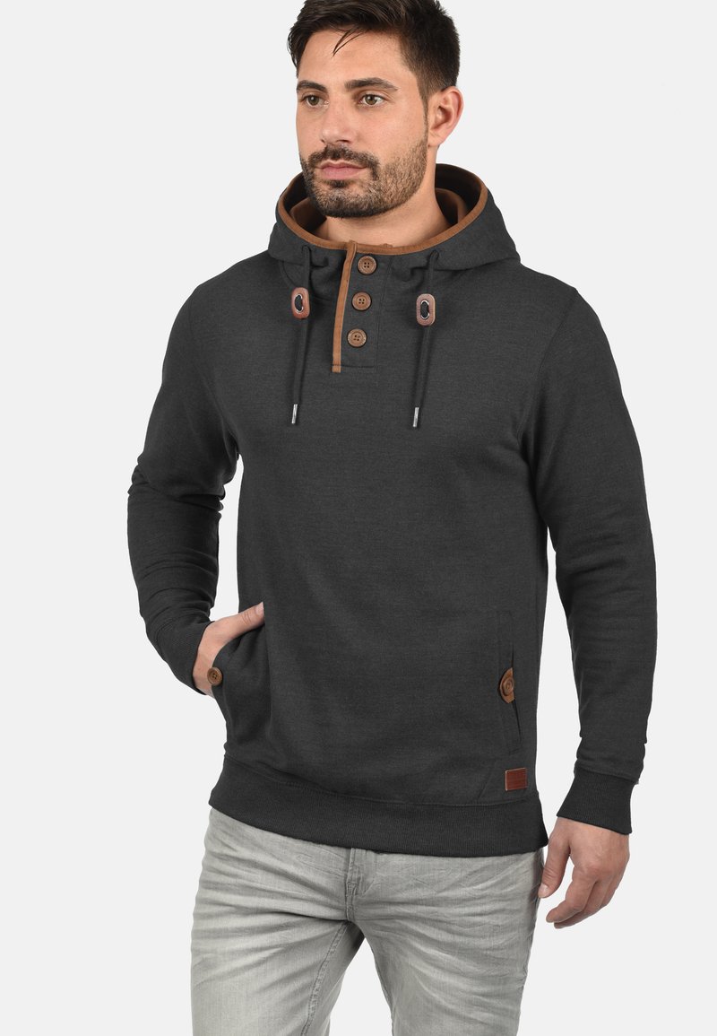 Mørk grå hettegenser laget av myk stoff, med en brun detalj rundt hetta og knappene, med justerbar snor og lommer foran.