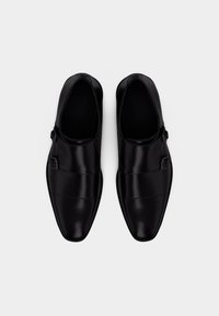 Μαύρα δερμάτινα παπούτσια με κομψό, μυτερό σχέδιο, με δύο αγκράφες και διακριτικές ραφές στην επιφάνεια.