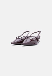 Chaussures slingback brillantes bordeaux foncé à talons bas, bouts pointus et fines brides réglables autour de la cheville sur fond blanc.