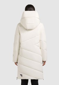 Geacă puffer albă cu un design quilted diagonal, glugă mare, mâneci lungi și fermoare laterale. Prezentă un logo pe partea stângă jos.