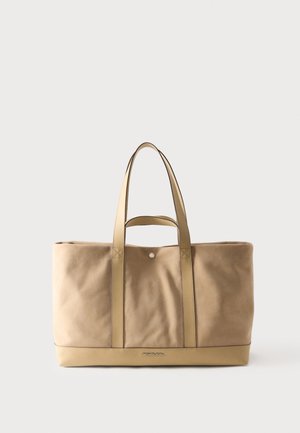 Beige large leather tote bag with double shoulder straps, snap closure, and Michael Kors logo on front bottom center.