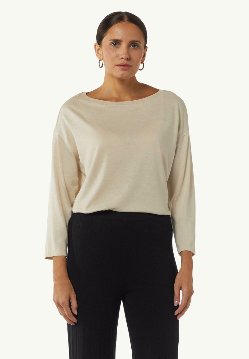 Beige, locker sitzendes Oberteil mit weitem Halsausschnitt und langen Ärmeln, aus weichem Stoff, kombiniert mit schwarzen, gerippten High-Waist-Hosen.