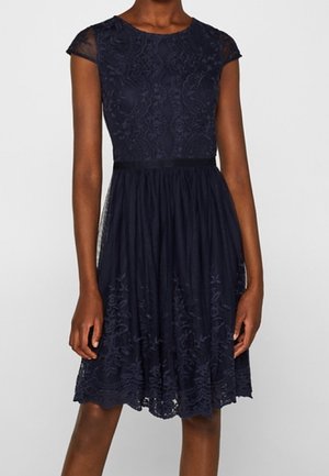 Tmavě modré šaty s krátkými průsvitnými rukávy typu cap. Mají květinový krajkový korzet a strukturovanou sukni, v pase stažené decentním páskem.