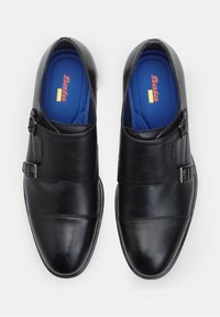 Zapatos de cuero negro con un acabado suave, que presentan dos hebillas ajustables y un diseño cosido. En el interior tienen plantillas azules con el logo.
