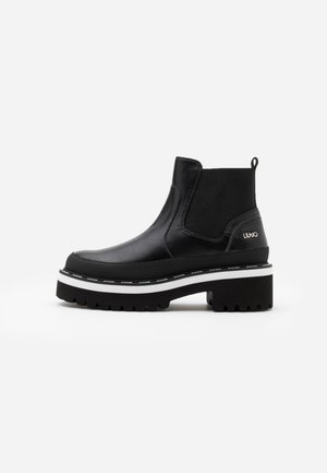 Black leather ankle boot with chunky platform sole, white stripe detail, elastic side panel, and pull tab at heel.
