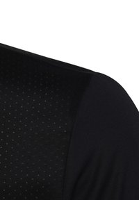 Camisa atlética negra con un patrón texturizado que presenta pequeños agujeros en una sección, material liso en otra sección y un corte ajustado.