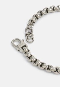 Pulsera de cadena de acero inoxidable con un acabado brillante, que presenta eslabones entrelazados y un cierre de langosta. Destacada por un eslabón circular.