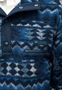 Μπλε και μαύρο φλις μπουφάν Columbia με μοτίβο, με τσέπη με φερμουάρ και κλείσιμο με κουμπιά πάνω από λευκό πουκάμισο.