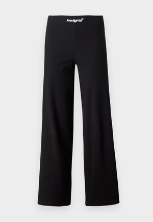 Pantalones de pierna ancha negros con una cintura elástica que presenta texto de logo en blanco. Fabricados con una tela suave y elástica, apta para el uso casual.