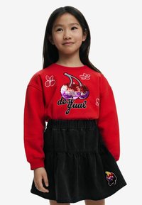 Sudadera roja con diseño de cereza de lentejuelas y acentos florales, combinada con una falda negra de volantes con un detalle bordado.