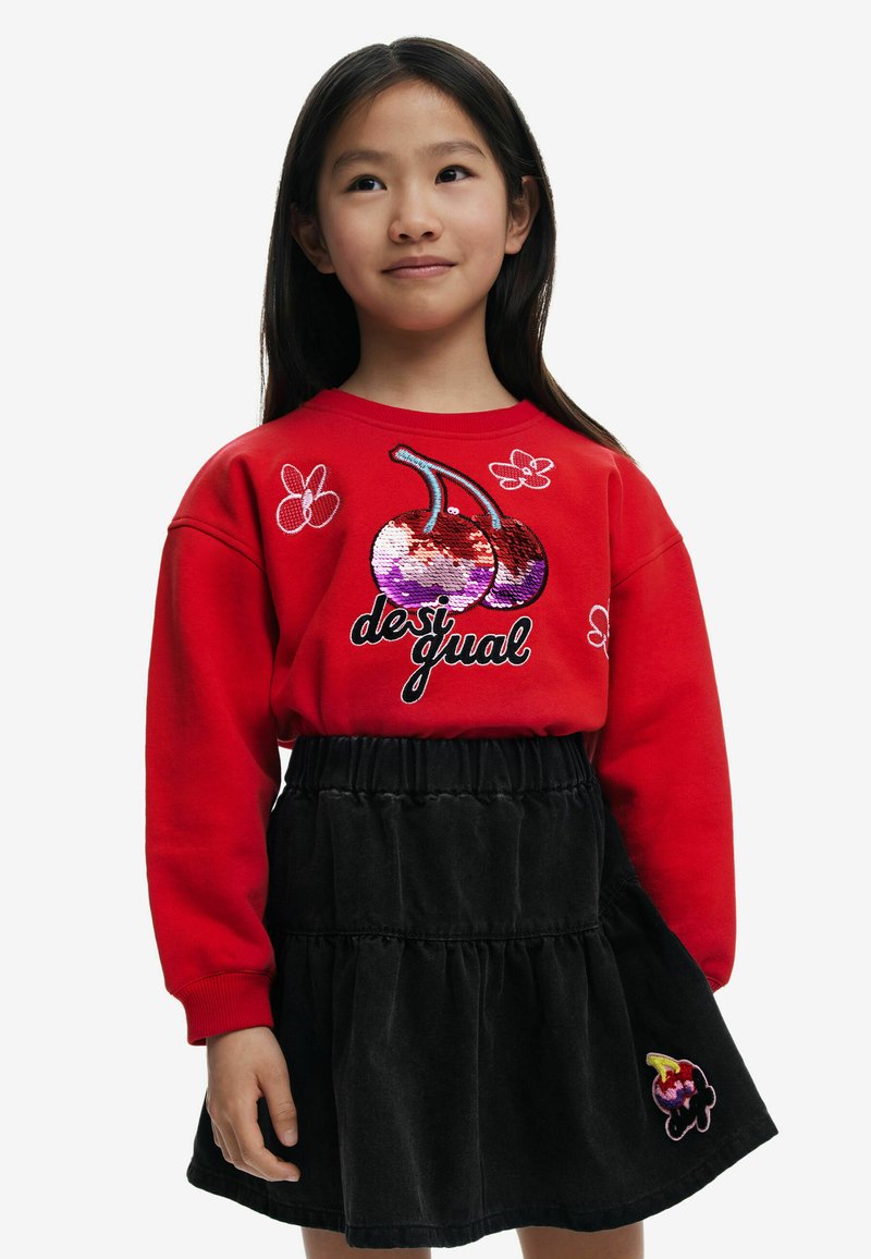 Sudadera roja con diseño de cereza de lentejuelas y acentos florales, combinada con una falda negra de volantes con un detalle bordado.