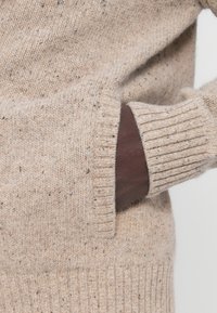 Beežimustriline kampsun soonikkoes varrukaotste ja tasku juures tumepruuni aktsendiga, pehme kootud tekstuuriga.