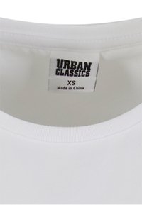 Balta kokvilnas t-krekls ar apaļu kakla izgriezumu. Uz etiķetes rakstīts "URBAN CLASSICS", izmērs XS, un norādīts "Ražots Ķīnā".
