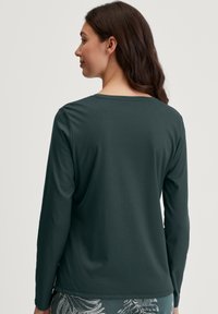 Donkergroene longsleeve top met een ronde halslijn, een soepele textuur en een ontspannen pasvorm. Het ontwerp heeft een lichte dip aan de achterkant van de zoom.