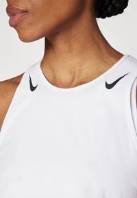 Hvid atletisk tanktop med rund halsudskæring og sorte Nike swoosh detaljer på hver skulder. Glat, let stof med en tætsiddende pasform.