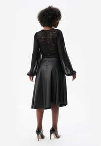Czarna koronkowa bluzka z długimi przezroczystymi rękawami, w połączeniu z czarną spódnicą z ekoskóry o rozkloszowanym kształcie i zamek błyskawiczny na plecach.