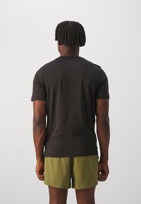 Černé tričko s krátkým rukávem a kulatým výstřihem, spárované s olivově zelenými šortkami. Materiál vypadá hladce a má přiléhavý střih.