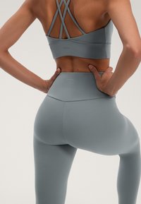 Svetlošedý športový podprsenka s prekríženými ramienkami a legíny s vysokým pásom, oboje vyrobené z hladkého, elastického materiálu s jemným brandingom.