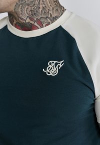 Blauw en crèmekleurig t-shirt met korte mouwen en een geribbelde ronde hals, voorzien van een geborduurd logo op de linkerborst en een soepele katoentextuur.