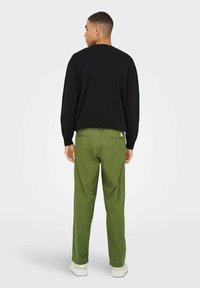 Un pull noir avec un col �à côtes, associé à un pantalon vert ample. La tenue présente un design épuré et un style décontracté.