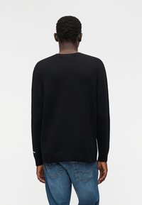 Μαύρο πλεκτό πουλόβερ με στρογγυλή λαιμόκοψη και μακριά μανίκια. Διαθέτει απλό σχέδιο, ομαλή υφή και ελαφριά ριμπ υφή στο λαιμό.