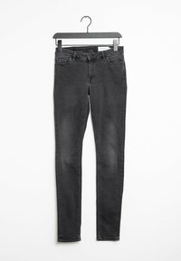 Musta skinny farkut roikkumassa mustassa ripustimessa valkoista taustaa vasten, jossa näkyvät etutaskut ja nappisulku.