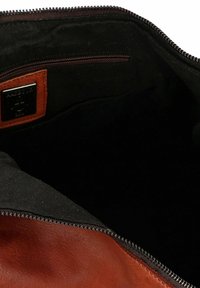 Intérieur d'un sac en cuir marron avec doublure en tissu foncé et une poche zippée. Comprend une étiquette en cuir de marque et des embellissements en argent.