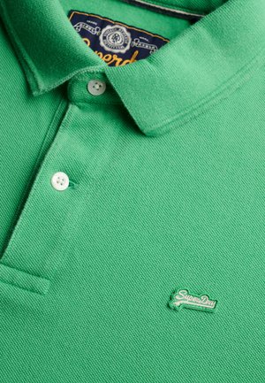 Groen poloshirt gemaakt van gestructureerde stof. Voorzien van een kraag, drie knopen en een klein geborduurd "SuperDry"-logo in het groen.