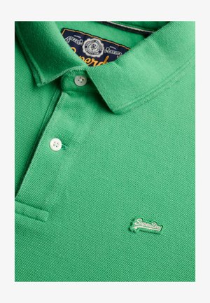 Groen poloshirt gemaakt van gestructureerde stof. Voorzien van een kraag, drie knopen en een klein geborduurd "SuperDry"-logo in het groen.