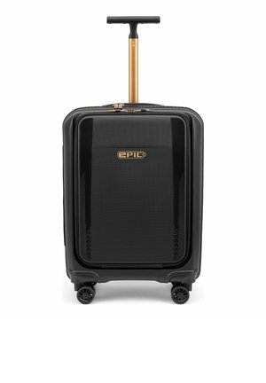 Valise rigide noire avec poche avant, poignée télescopique dorée, quatre roues doubles pivotantes et logo "EPIC" sur le panneau avant.