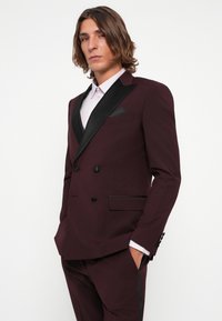 Burgundy double-breasted suit jacket with black satin accents, peaked lapel, and matching trousers. Features a textured finish and tailored fit.