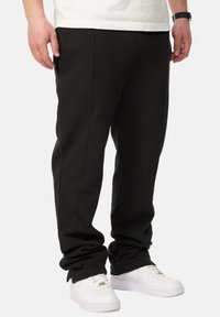 Schwarze Jogginghosen aus weichem Stoff mit flachen Nähten, elastischen Bündchen und seitlichen Taschen, kombiniert mit weißen Sneakers.