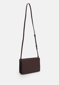 Ciemnobrązowa skórzana torba na ramię o gładkiej teksturze, prostokątnym kształcie, regulowanym pasku i minimalistycznym designie.