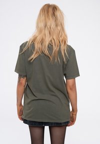 Olive green oversized t-shirt in soft cotton, short sleeves, round neckline, and a relaxed fit, featuring visible stitching and a smooth texture.