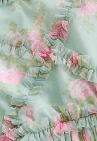 Tissu vert clair avec un motif floral rose et jaune, présentant des bords froncés et des accents dans tout le design. Texture douce et légère.