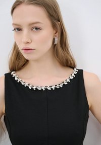 Vestido negro con un escote de joyas que presenta piedras claras y brillantes. Suave tela y silueta ajustada realzan el diseño elegante.