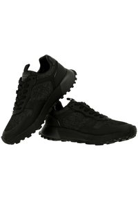 Paire de baskets de sport noires avec fermeture à lacets et panneaux en tissu texturé, une chaussure reposant sur l’autre sur fond blanc.