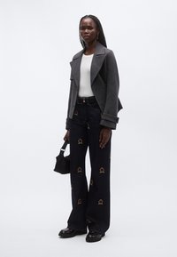 Hall villasegu segatud jakk, valge pikutiistunud särk, tumedad teksased, mis on alt laienevad ja millel on värvikas krooni tikand, must vöö ja väike must käekott.