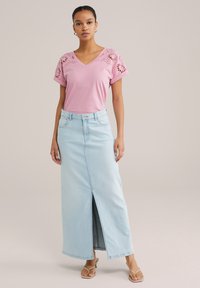Tricou din bumbac roz deschis, cu modele florale brodate pe mâneci, asortat cu o fustă din denim albastru deschis, lungime până la glezne, cu o fanta frontală.