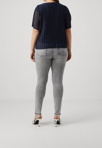 Marine gestreepte top met korte mouwen en een effen rug, gecombineerd met grijze aansluitende jeans en zilveren hoge hakken. Gevoelige stofdetails zichtbaar.