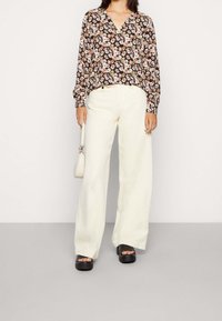 Blusa floreale con sfondo nero, maniche lunghe e scollatura a V. Abbinata a pantaloni crema a gamba larga e sandali platform neri spessi.