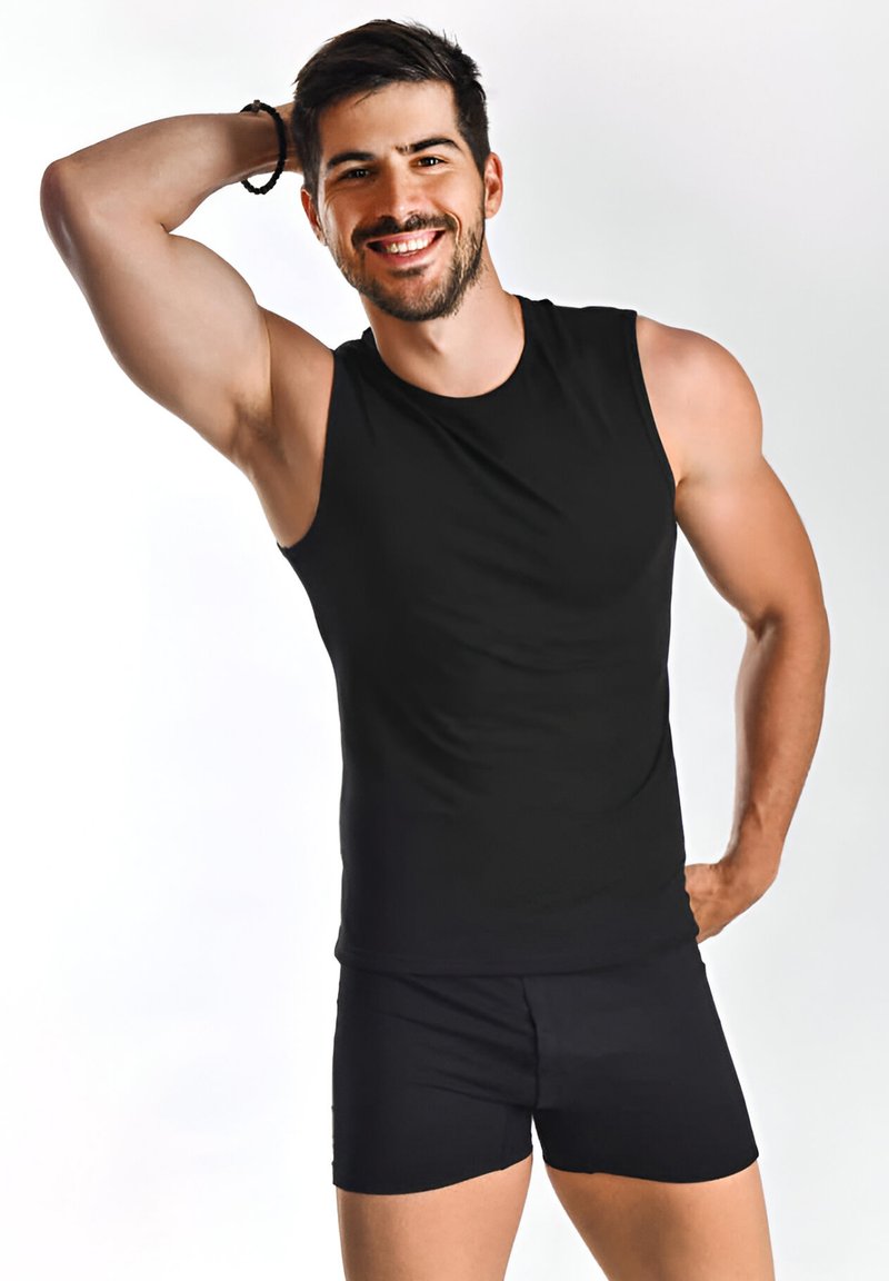 Schwarzes ärmelloses Shirt aus glattem Stoff, kombiniert mit passenden schwarzen Shorts; die enganliegende Passform betont den muskulösen Körperbau vor einem hellen Hintergrund.