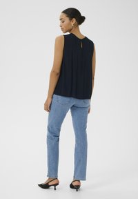 Haut sans manches bleu marine avec un détail de dos en trou de serrure, associé à un jean droit bleu clair et des mule à talons noirs. Texture de tissu lisse.