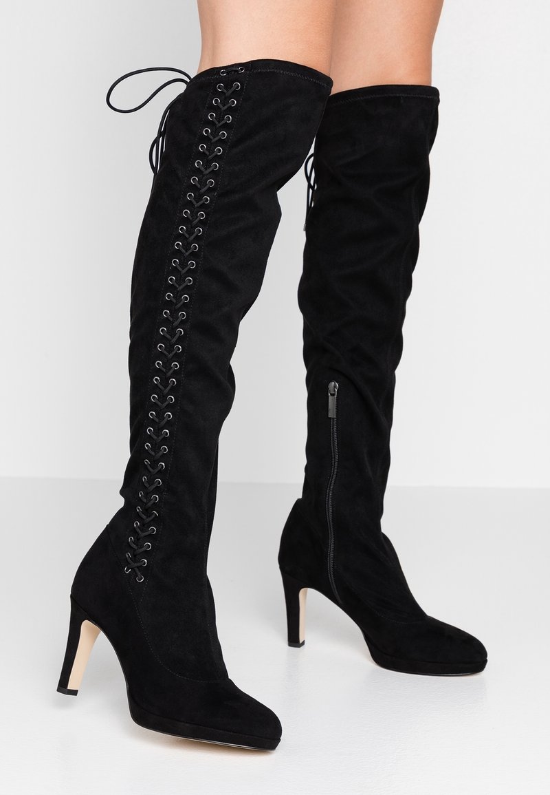 Bottes noires en daim montantes jusqu'à la cuisse avec une fermeture éclair sur le côté, présentant un laçage vertical sur le côté extérieur et un talon aiguille.