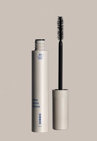 Ljusbeige mascaraförpackning med blå text, med ett strukturerat lock. Svart mascaraborste visas bredvid, med täta borst för volym.