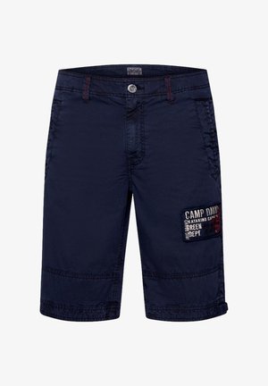 Shorts bleu marine en tissu léger, comportant un patch avec du texte rouge et blanc sur le côté et des détails de couture contrastants.