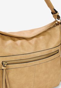 Borsa a tracolla in finta pelle color sabbia, con un design morbido, dotata di una tasca con zip e dettagli in hardware dorato. Texture liscia e dettagli di cucitura discreti.